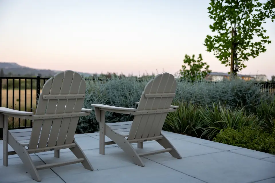 Smooth concrete patio with two wooden Adirondack chairs at sunset