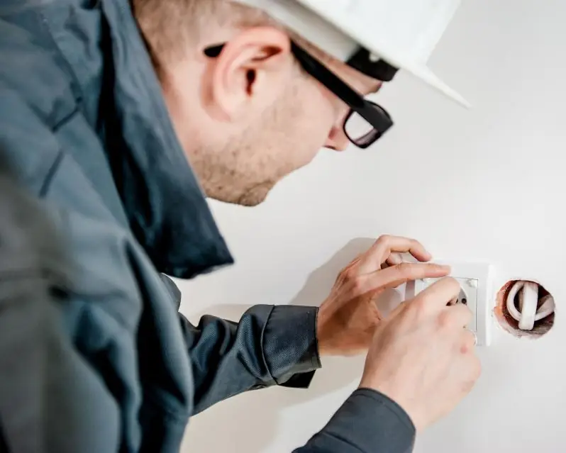 Electrician in a hard hat installing a wall outlet