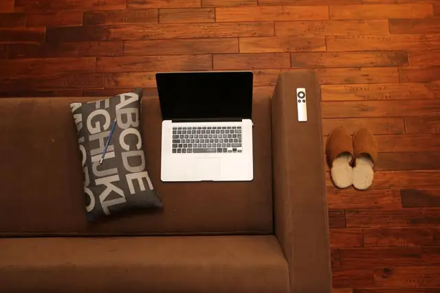 Couch and laptop on a reddish hardwood floor