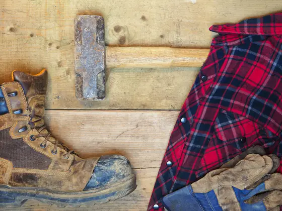 Work boots, gloves, a hammer and a flannel shirt on a wood bench