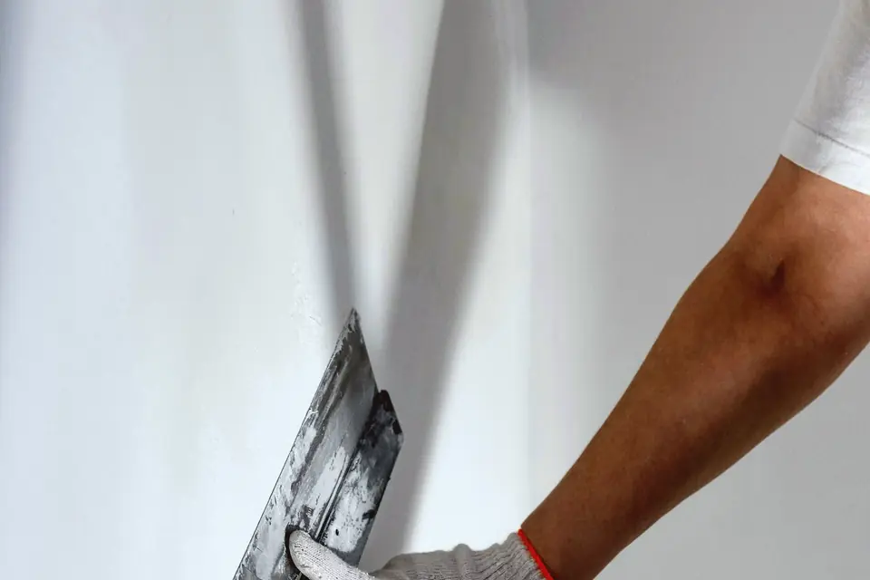 Gloved hand smoothing a wall patch with a trowel
