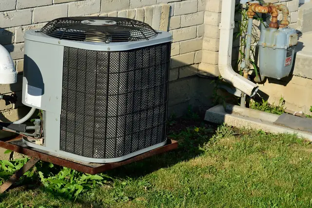 Outdoor AC condenser unit next to a brick house