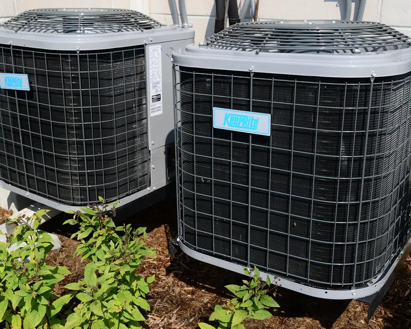 Two outdoor AC condenser units beside a house
