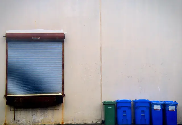 Row of blue recycling bins under a metal shutter