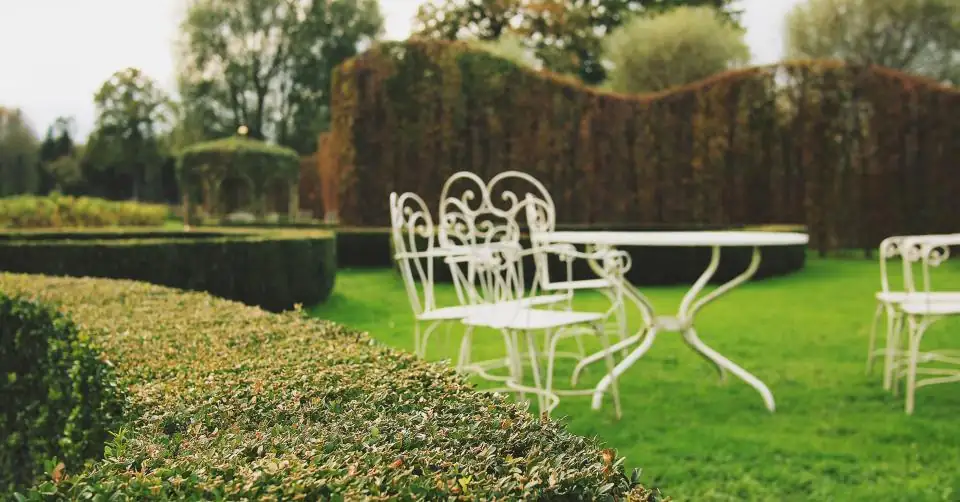 Neatly trimmed hedges and lawn around a white garden table and chairs