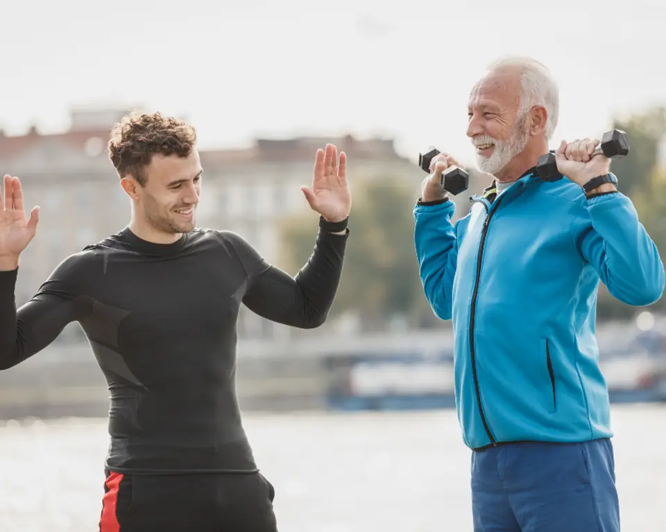 Trainer coaching an older client through a dumbbell press outdoors