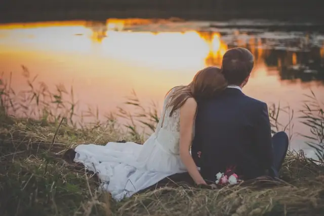 Couple in wedding clothes sitting together at sunset