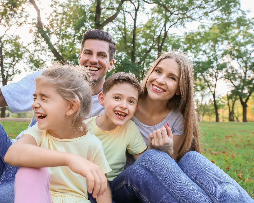 Family of four laughing together on a blanket in a park