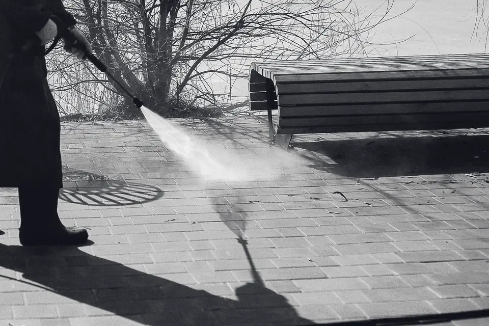 Black-and-white photo of a pressure-washer wand spraying brick pavers, leaving a wet strip