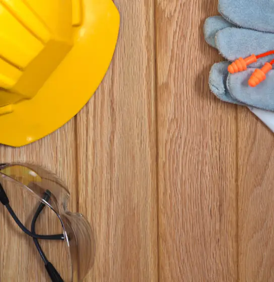 Yellow hard hat, safety glasses and work gloves on a wood deck