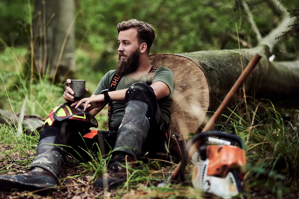 Arborist sitting by a felled log with a chainsaw in the woods